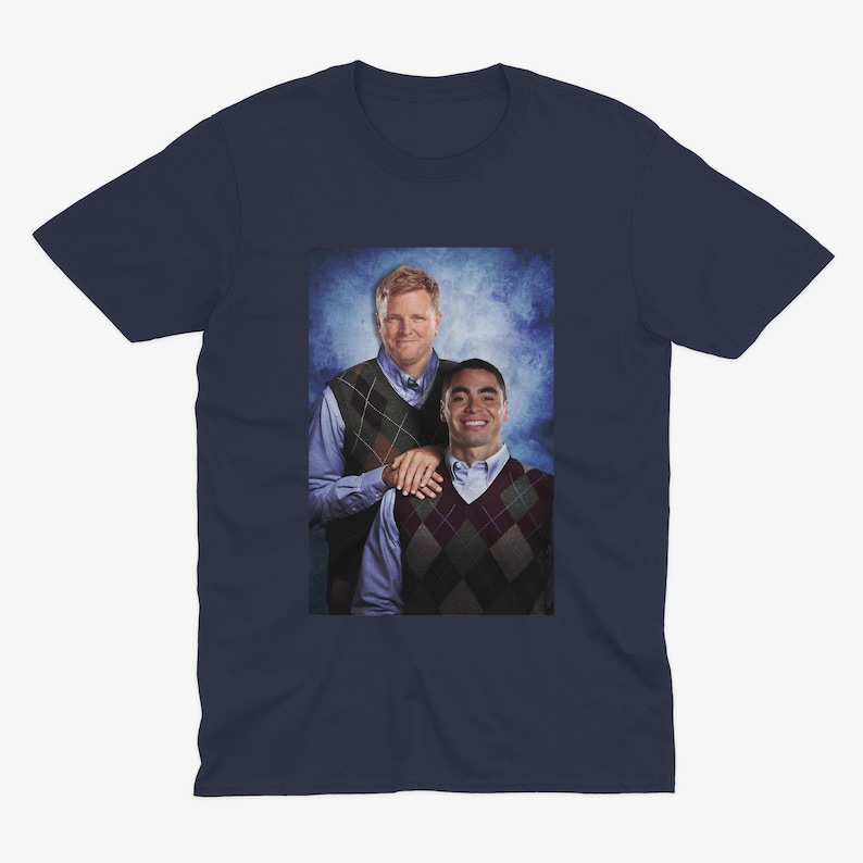 Peut inclure: Un t-shirt bleu marine avec une photo de deux hommes portant des pulls. L'homme &agrave; gauche porte un pull &agrave; motifs vert et marron et l'homme &agrave; droite porte un pull &agrave; motifs marron et blanc.