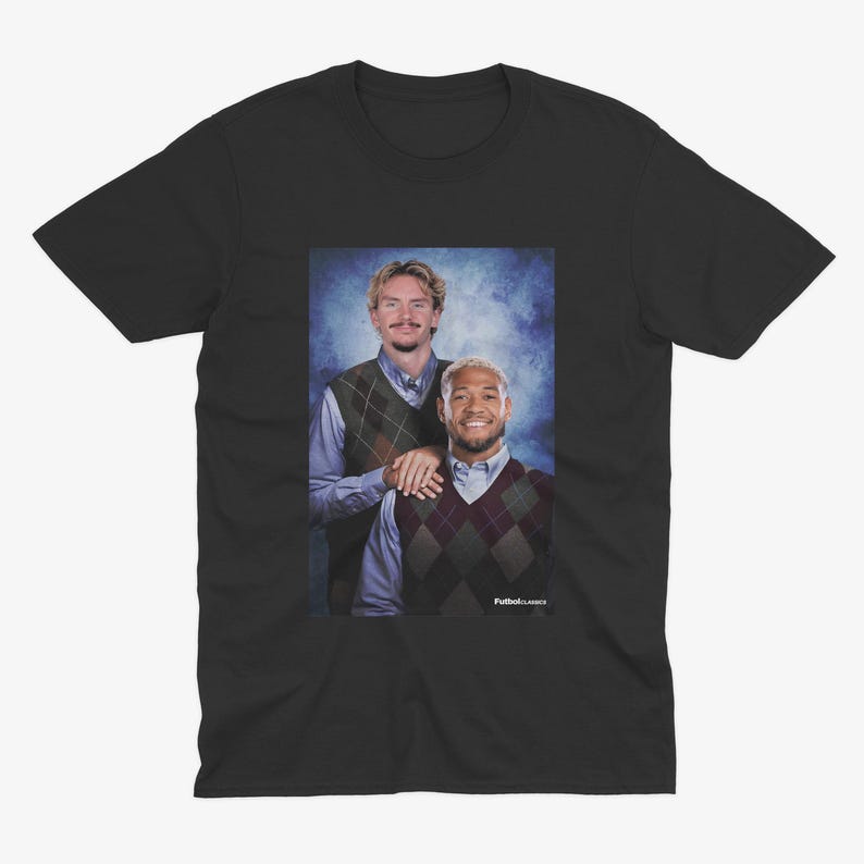 May include: Black t-shirt featuring a portrait of two men wearing argyle vests over button-down shirts. The image has a blue background and the text "FutbolClassics" is visible.