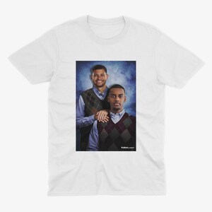 May include: A white t-shirt featuring a photograph of two men wearing sweaters. The men are standing in front of a blue and white background. The text "Putback Classics" is at the bottom of the photo.