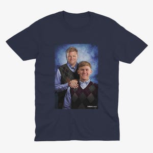 Pu&ograve; includere: Una t-shirt blu navy con una foto di due uomini con maglioni. L'uomo a sinistra indossa un maglione a motivi blu e bianchi, mentre l'uomo a destra indossa un maglione a motivi bordeaux e bianchi. Il testo "Puttin' on Classics" &egrave; in basso nella foto.