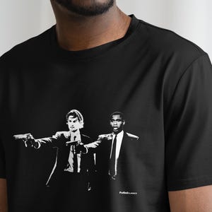 May include: Black t-shirt featuring a white graphic print of two men in suits, one pointing a gun. The text "Pulp Fiction" is printed at the bottom of the graphic.