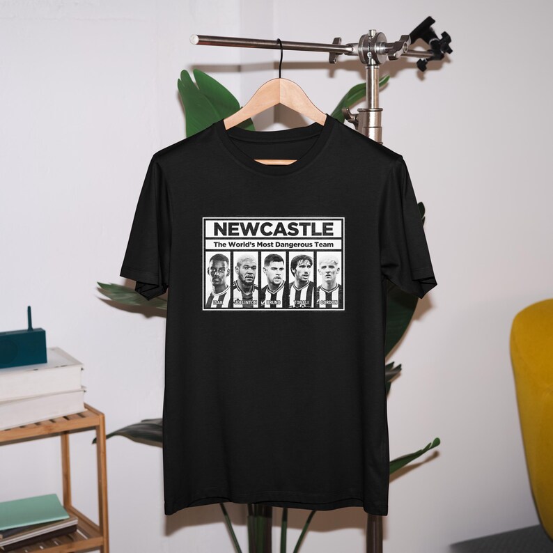 K&ouml;nnte beinhalten: Schwarzes T-Shirt mit einer wei&szlig;en Grafik von f&uuml;nf Fu&szlig;ballspielern und dem Text "NEWCASTLE The World's Most Dangerous Team".