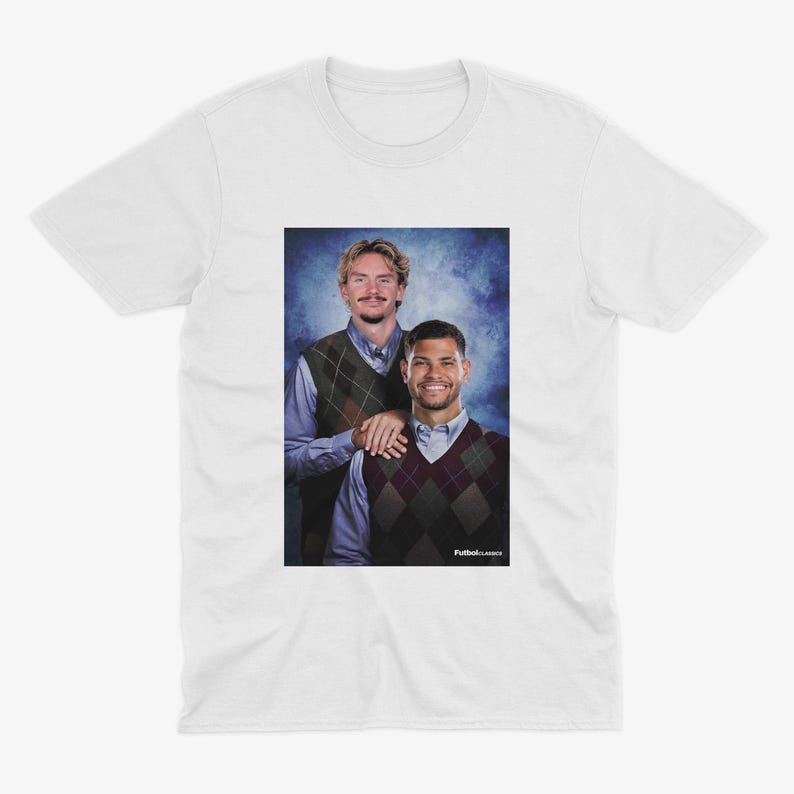 May include: White t-shirt featuring a portrait of two men wearing argyle vests over button-down shirts. The image has a blue background and the text "Futbol Classics" is visible in the bottom right corner.