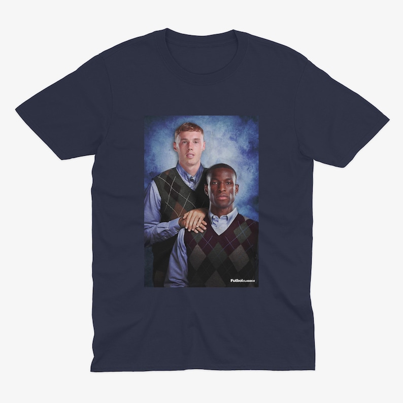 May include: A navy blue t-shirt featuring a photo of two men in sweaters. The men are standing next to each other and smiling. The background is a blue and white gradient.