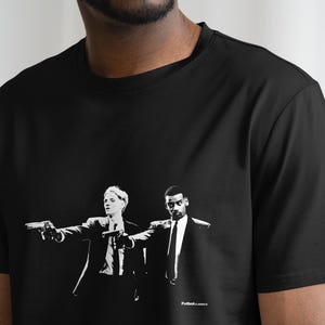 Puede incluir: Camiseta negra con un estampado gr&aacute;fico blanco de dos personas sosteniendo armas de fuego. El gr&aacute;fico es una escena de la pel&iacute;cula Pulp Fiction.