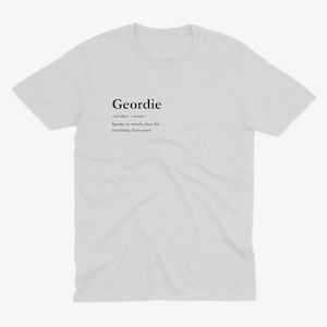 Puede incluir: Camiseta blanca con la definici&oacute;n de "Geordie" impresa en negro. La definici&oacute;n incluye la pronunciaci&oacute;n, la categor&iacute;a gramatical y una descripci&oacute;n del dialecto y estilo de vida Geordie.