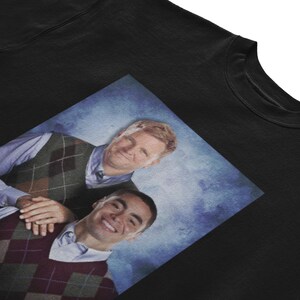 Peut inclure: Un sweat-shirt noir avec une image imprim&eacute;e de deux hommes portant des pulls en argyle. Les hommes sourient et semblent &ecirc;tre amis. L'image est sur un fond bleu.