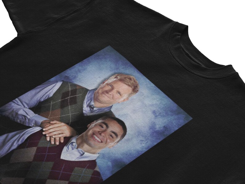 Peut inclure: Un sweat-shirt noir avec une image imprim&eacute;e de deux hommes portant des pulls en argyle. Les hommes sourient et semblent &ecirc;tre amis. L'image est sur un fond bleu.