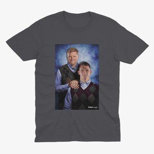 Op de afbeelding: Een donkergrijs T-shirt met een foto van twee mannen die truien dragen. De mannen staan ​​naast elkaar en glimlachen. De tekst "Fullback Classics" staat onderaan de foto.