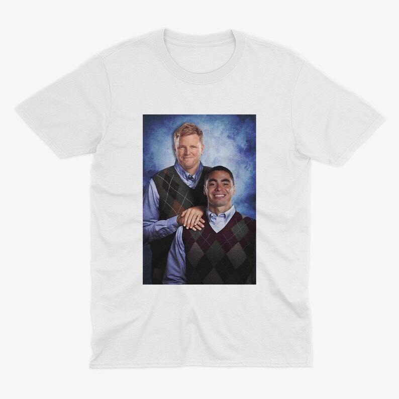 Peut inclure: Un t-shirt blanc avec une photo de deux hommes portant des pulls. L'homme &agrave; gauche porte un pull &agrave; motifs vert et blanc et l'homme &agrave; droite porte un pull &agrave; motifs rouge et blanc.