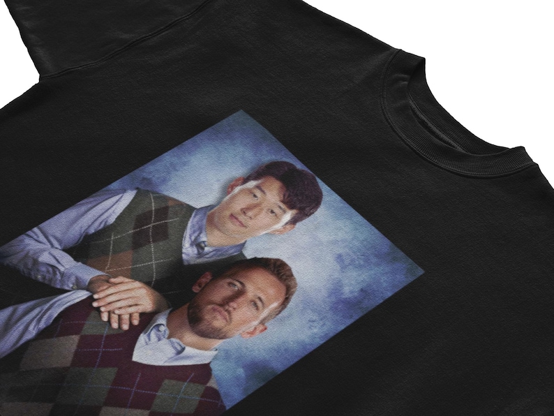 Op de afbeelding: Een zwart sweatshirt met een bedrukte afbeelding van twee mannen die geruite vesten dragen. De mannen lachen en kijken naar de camera. De achtergrond is een blauwe en witte gradi&euml;nt.
