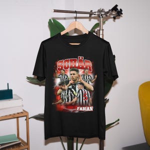 May include: Black t-shirt featuring a retro-style graphic of a football player, Fabian Sch&auml;r, wearing a black and white jersey with the number 5. The graphic includes the text "Sch&auml;r" and "Fabian".