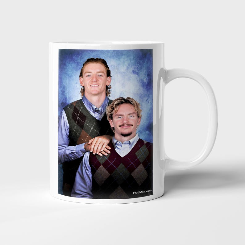 May include: White ceramic mug featuring a portrait of two people wearing argyle vests over button-down shirts. The image has a blue background and the text "FutbolClassics" is printed on the mug.