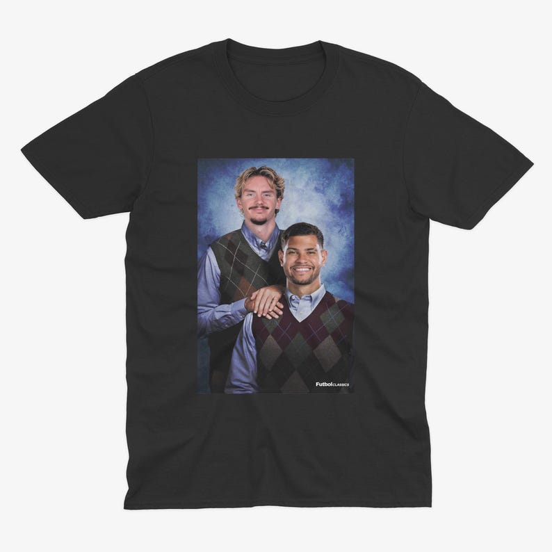 May include: Black t-shirt featuring a portrait of two men wearing argyle vests over button-down shirts. The image has a blue background and the text "FutbolClasico" is visible in the bottom right corner.