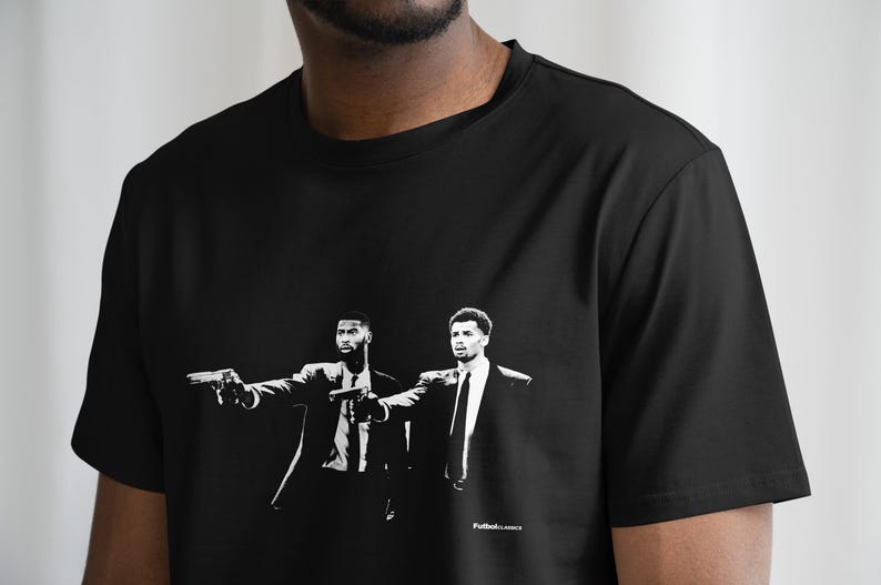 Op de afbeelding: Zwart-wit T-shirt met een grafische print van twee mannen in pak die met pistolen naar de kijker wijzen. De tekst "Pulp Fiction" staat onderaan het shirt.