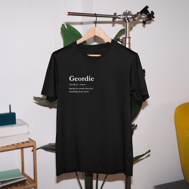 Puede incluir: Camiseta negra con la palabra "Geordie" en blanco y una definici&oacute;n. La definici&oacute;n dice: "Habla en vocales, vive para el d&iacute;a del partido, no teme nada."