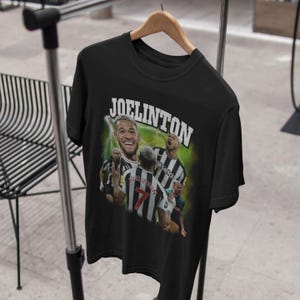 Pode incluir: Camiseta preta com uma estampa gr&aacute;fica de um jogador de futebol, Joelinton, com um uniforme preto e branco. O texto "JOELINGTON" est&aacute; impresso em letras brancas na camiseta.