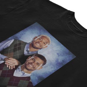 K&ouml;nnte beinhalten: Ein schwarzes Sweatshirt mit einem Grafikdruck von zwei M&auml;nnern, die Argyle-Pullover tragen. Die M&auml;nner l&auml;cheln und scheinen Freunde zu sein. Der Hintergrund ist ein blauer und wei&szlig;er Farbverlauf.