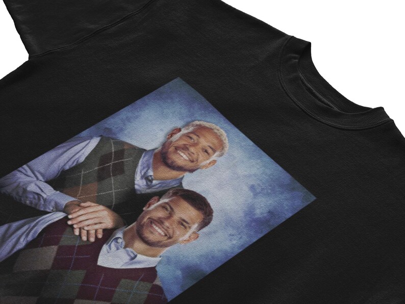 K&ouml;nnte beinhalten: Ein schwarzes Sweatshirt mit einem Grafikdruck von zwei M&auml;nnern, die Argyle-Pullover tragen. Die M&auml;nner l&auml;cheln und scheinen Freunde zu sein. Der Hintergrund ist ein blauer und wei&szlig;er Farbverlauf.