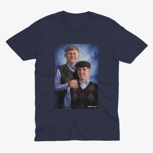 Pu&ograve; includere: Una t-shirt blu navy con una foto di due persone che indossano maglioni. La foto &egrave; su uno sfondo blu e bianco. Il testo "Puttin' on Classics" &egrave; in basso nella foto.