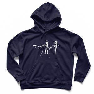 May include: Navy blue hoodie featuring a white graphic of two men pointing guns. The hoodie has a drawstring hood and a kangaroo pocket. The graphic is a stylized image of a scene from a movie.