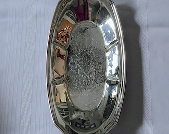 Könnte beinhalten: Ein ovales Serviertablett aus Silber mit einem verzierten Design. Das Tablett hat einen leicht erhöhten Rand und eine glatte, reflektierende Oberfläche.