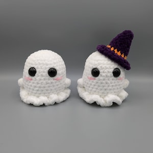 May include: Two crocheted ghost ornaments, one wearing a purple witch hat with orange accents. Both ghosts have black eyes and pink cheeks.