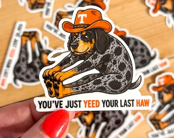 May include: A die-cut sticker featuring a black and grey spotted hound dog wearing an orange cowboy hat with a white T logo. The dog is stretching forward with a wheat stalk in its mouth. Below the dog, the text reads YOU'VE JUST YEED YOUR LAST HAW.