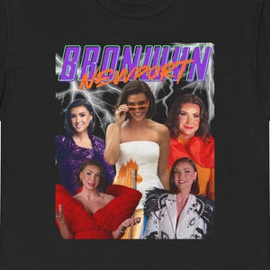 Puede incluir: Camiseta negra con un gráfico de estilo retro que presenta el texto "Braunwyn Newport" en morado y naranja con rayos. El gráfico también incluye cinco mujeres en diferentes poses.