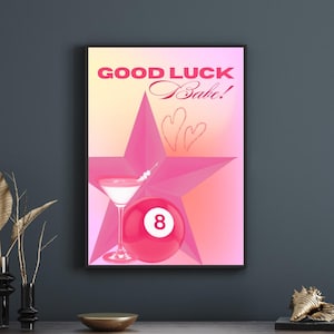May include: Framed print with a pink star, martini glass, and a red eight-ball. The text "GOOD LUCK Babe!" is in pink. The artwork has a gradient background and is displayed on a dark wall. A decorative piece.
