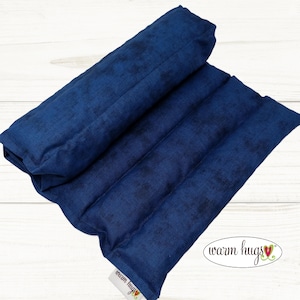 May include: A blue fabric heating pad with a white label that says "warm hugs" with a red heart. The pad is folded in half and has a textured surface.