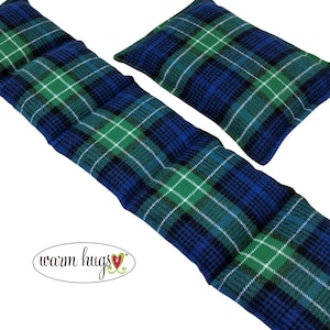 May include: Two plaid heating pads in blue, green, black, and white. One is long and rectangular, and the other is a smaller square shape. The pads have a quilted design. The words "warm hugs" are in a cursive font.