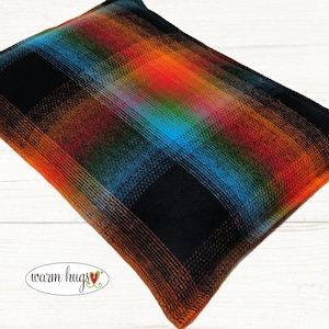 May include: A rectangular pillow with a plaid pattern in black, orange, red, blue, and green. The pillow has a black border and the words "warm hugs" in a cursive font.