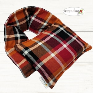 May include: A red, orange, black, and white plaid fabric neck wrap with a sewn-in pocket. The neck wrap is made by "warm hugs" and has a label on the bottom.