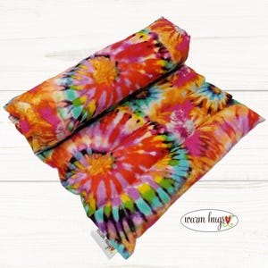 May include: A tie-dye patterned microwave heating pad with the text "warm hugs" on the bottom right corner.