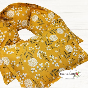 May include: Mustard yellow heating pad with a floral pattern of white flowers and black stems. The pad is rectangular and curved, with the text "warm hugs" in a white script font.
