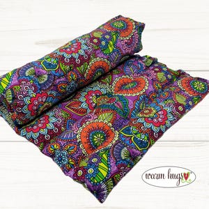 May include: Two colorful, patterned fabric items. One is rolled, the other is flat. The fabric features a vibrant paisley design with purple, orange, green, and blue hues. The items are likely part of a home decor or comfort product line.