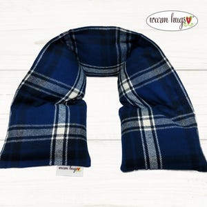 May include: A blue plaid neck wrap with the text "warm hugs" in a cursive font. The wrap is made of a soft fabric and has a rectangular shape with two padded sections. The plaid pattern includes white and black lines.