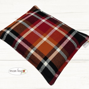 May include: Red, orange, black, and white plaid fabric heating pad with the text "warm hugs" on the bottom left corner and "warm hugs" on the top right corner.