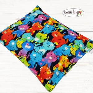 May include: A colorful cat-themed fabric heating pad with the text "warm hugs" in a heart shape.