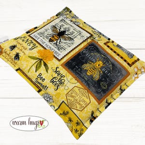 May include: Yellow fabric pouch with a bee theme. The pouch has a variety of bee-themed designs, including bees, honeycombs, and flowers. The text "Save the bees" is printed on the pouch. The pouch is made by "Warm Hugs".