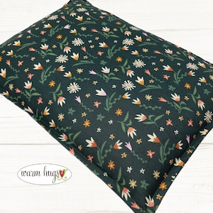 May include: A dark green fabric pillow with a floral pattern. The pattern features small white flowers, pink flowers, and orange flowers. The pillow has a white label with the text "warm hugs" in black.
