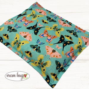 May include: A teal blue rectangular pillow with a butterfly pattern. The pillow is filled with buckwheat hulls and is designed to provide comfort and support.