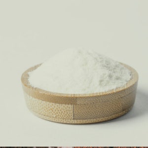 May include: A small, round bamboo bowl containing a pile of white powder. The bowl is a natural light brown colour with a textured exterior. The powder appears fine and fluffy, contrasting with the bowl's texture.