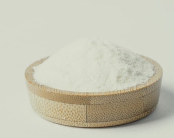 May include: A small, round, bamboo bowl filled with a mound of white powder. The bowl has a natural, light brown color with a textured exterior. The powder appears fine and fluffy, contrasting with the bowl's texture.
