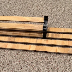 May include: A wooden shelf unit with four shelves and black plastic brackets. The shelves are made of light wood and the brackets are made of black plastic.