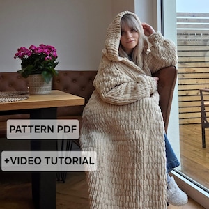 May include: A beige, chunky knit hooded cardigan with a textured, ribbed appearance. The garment features long sleeves and a full-length design. Text overlay on the image reads: PATTERN PDF +VIDEO TUTORIAL.