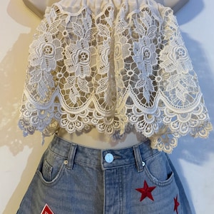 May include: A cream-colored lace tube top with a scalloped edge is paired with denim shorts. The shorts feature red star embroidery and a Budweiser patch. The outfit is displayed on a mannequin.