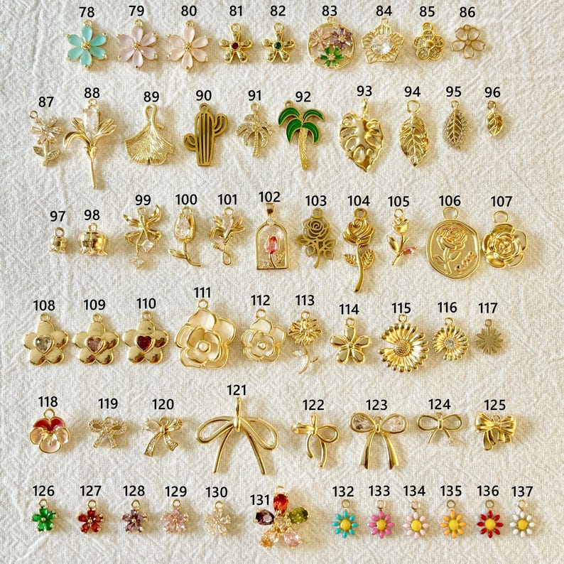 May include: A collection of gold-colored charms and pendants in various floral, leaf, and bow designs. Includes charms shaped like flowers, leaves, cacti, and bows. Some charms feature colorful accents, such as green, pink, and blue enamel.