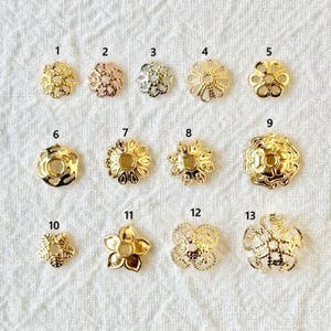 以下が含まれることがあります： 13個の金色の金属製の花型のジュエリーパーツのコレクション。パーツのデザインは様々で、透かし彫り、無地の花びら、詳細な中心部などがあります。これらのコンポーネントは、ジュエリー作りやクラフトに使用されます。